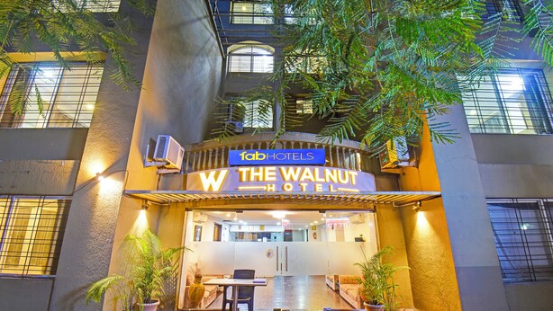 The exterior of The Walnut Hotel with a modern design, featuring a prominent entrance, potted plants, and a clear view of the interior through the glass doors. - Fabhotel The Walnut (Pune)