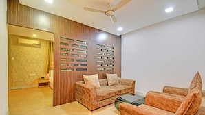 A modern living room with a sofa set, a glass coffee table, and a decorative wall panel. - Fabhotel The Walnut (Pune)