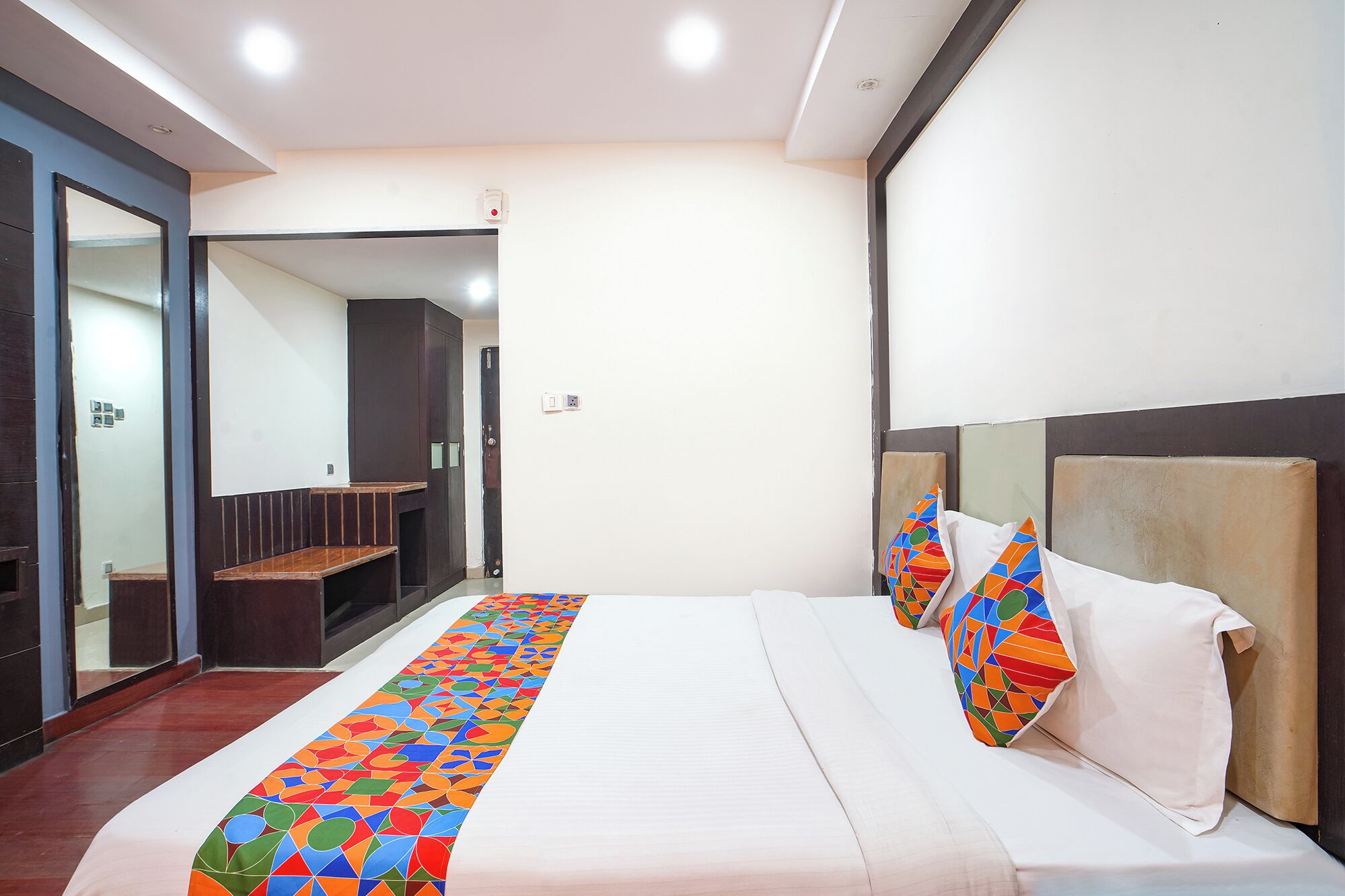 A hotel room with a bed, a bench, and a mirror.