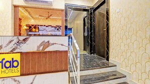 A hotel reception area with a marble reception desk, a staircase leading to an elevator, and a patterned wall.