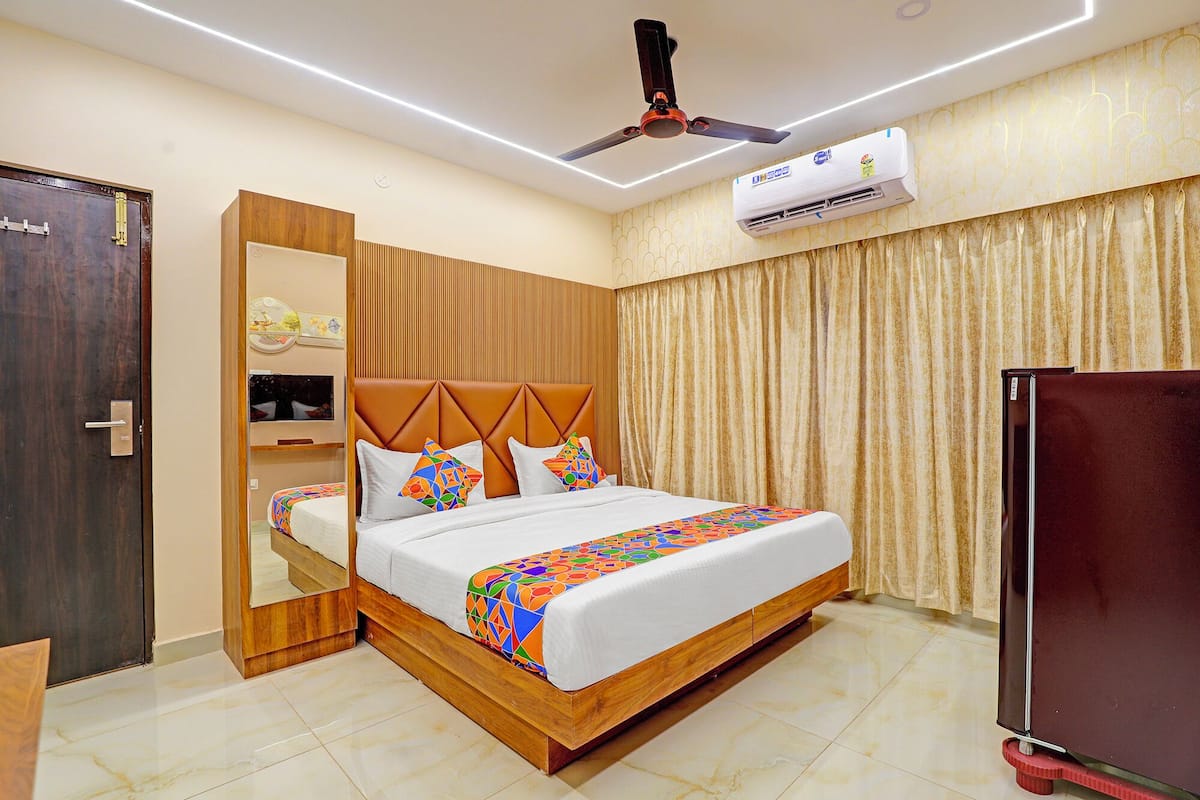 Une chambre d’hôtel avec un lit en bois, un ventilateur de plafond, un appareil de climatisation et un réfrigérateur.
