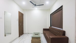 A room with a ceiling fan, a glass coffee table, a brown sofa, a large mirror, and a window with blinds. - Fabhotel Lake Vista (Indore)