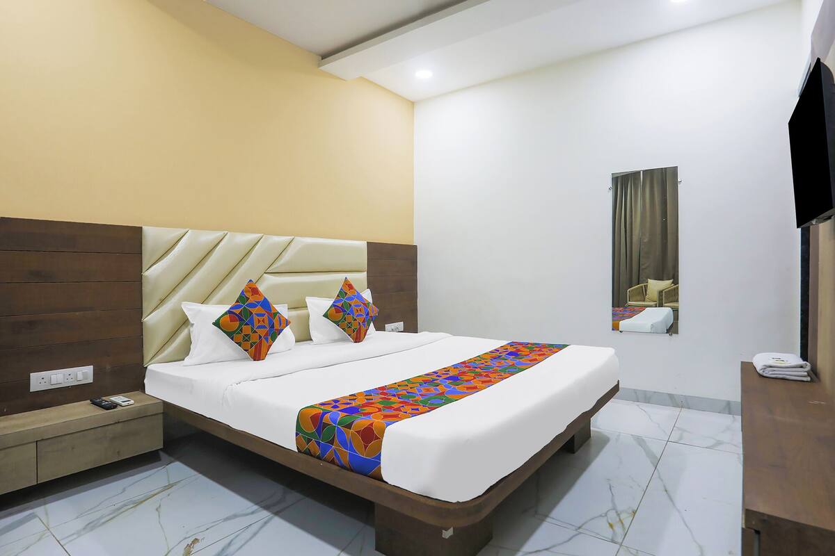 A hotel room with a bed, a nightstand, a TV, and a mirror.