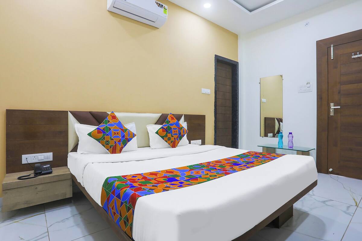 A hotel room with a large bed, a bedside table with a phone, a mirror, and a door.