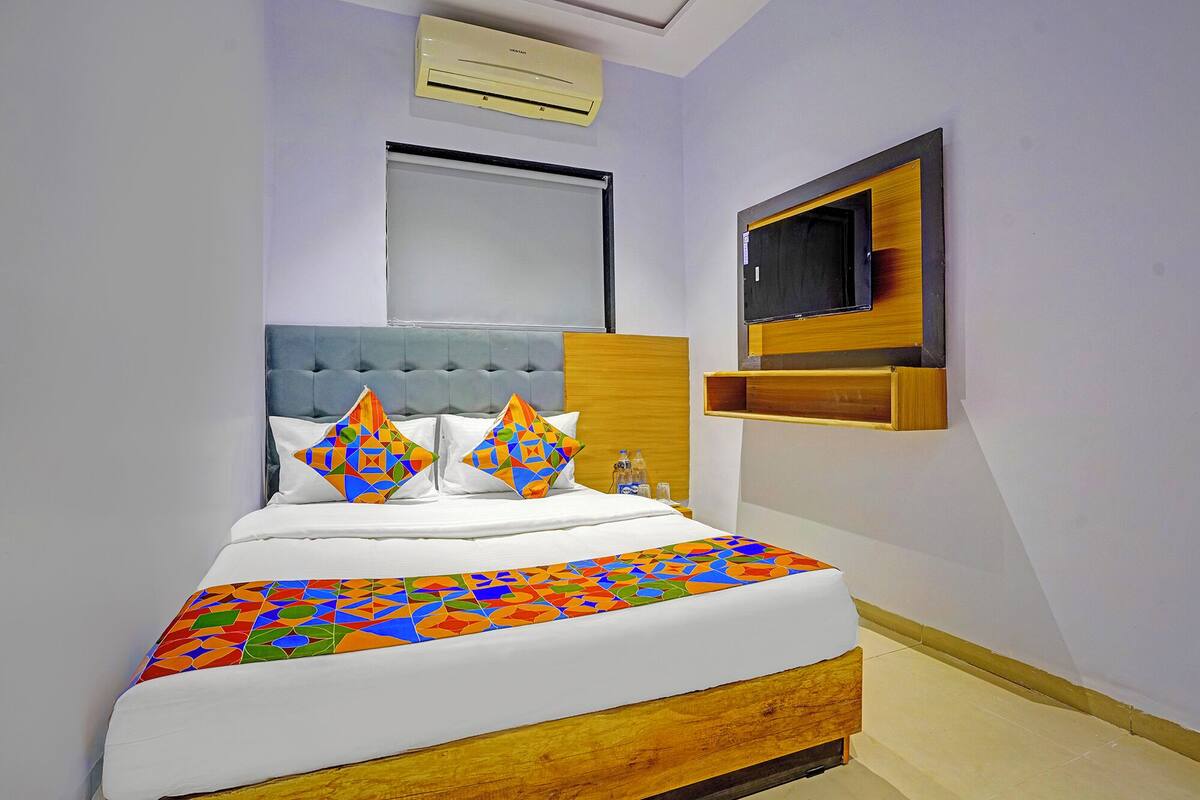 Quarto com cama, televisão fixada na parede e janela sobre a cama.