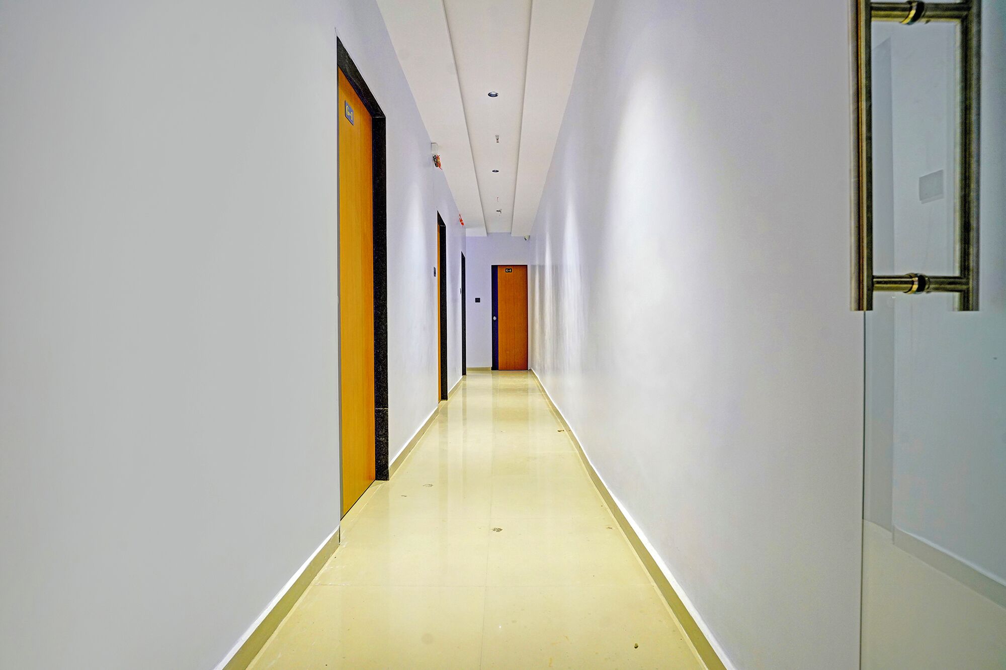 A long, narrow hallway with white walls and a yellow floor, leading to a door at the end.