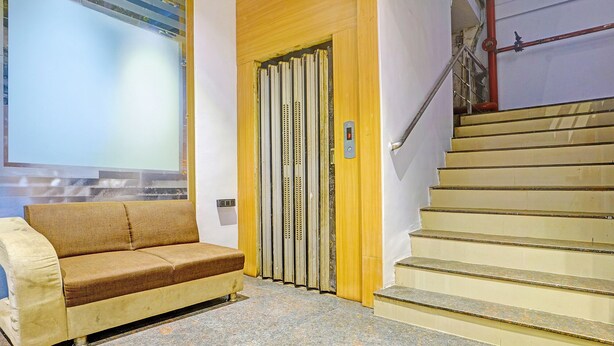 A hotel lobby with a sofa, a door with a vertical handle, and a staircase with a handrail. - Fabhotel Nidhivan Palace (Surat)
