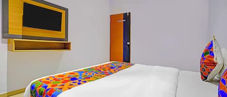 Una habitación de hotel con cama, cabecera de madera, televisor montado en la pared y una puerta.