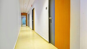 A long, narrow hallway with doors on one side and a clear view into a room at the end. - Fabhotel Nidhivan Palace (Surat)
