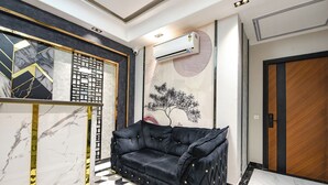 Een modern interieur met een zwarte leren bank, een decoratieve wand met een geometrisch patroon, en een grote airconditioning.