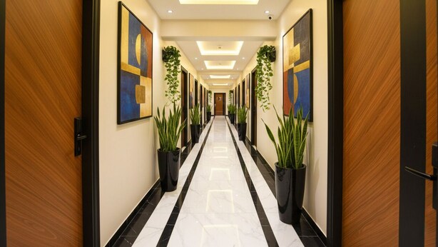 Een hotelgang met een zwart-wit marmeren vloer, houten deuren en kunstwerken in lijsten aan de muren.