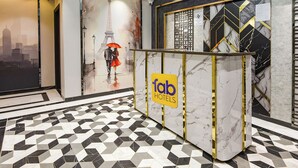 Een hotel receptie met een marmeren vloer, een receptiebalie met een 'fab hotels' bord en een muurschildering van een koppel met een paraplu.