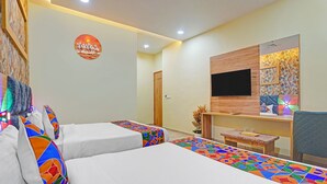 Ein Hotelzimmer mit zwei Betten, einem Fernseher, einem kleinen Tisch und einer Wandverzierung.