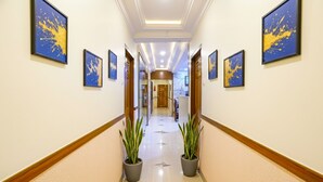 Un pasillo de hotel con cuadros enmarcados en las paredes, plantas en macetas y un suelo pulido.