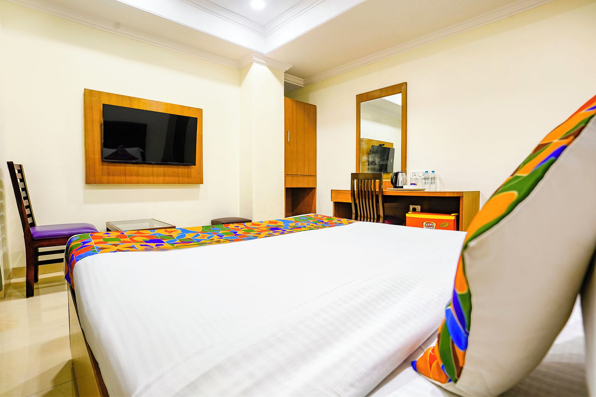 A hotel room with a bed, a desk, a chair, a television, and a mirror.