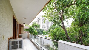 A balcony with a view of a tree-lined street and a building in the background. - FabHotel The Lalit Vibes - Nr. DLF Phase 2 & MG Road Metro (Gurugram)