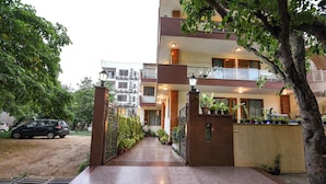 A multi-story building with a gated entrance, potted plants, and a paved pathway leading to the entrance.