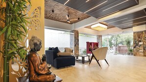 Un hall d’entrée spacieux, agrémenté d’une statue de Bouddha, de mobilier moderne et d’une grande fenêtre offrant une vue sur l’extérieur.