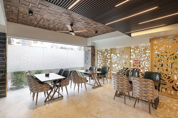 A modern dining area with a ceiling fan, patterned wall decor, and a view through a window.