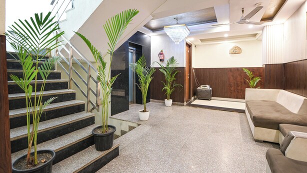 Un hall d’hôtel moderne avec un escalier, des plantes en pot, un lustre et un canapé.