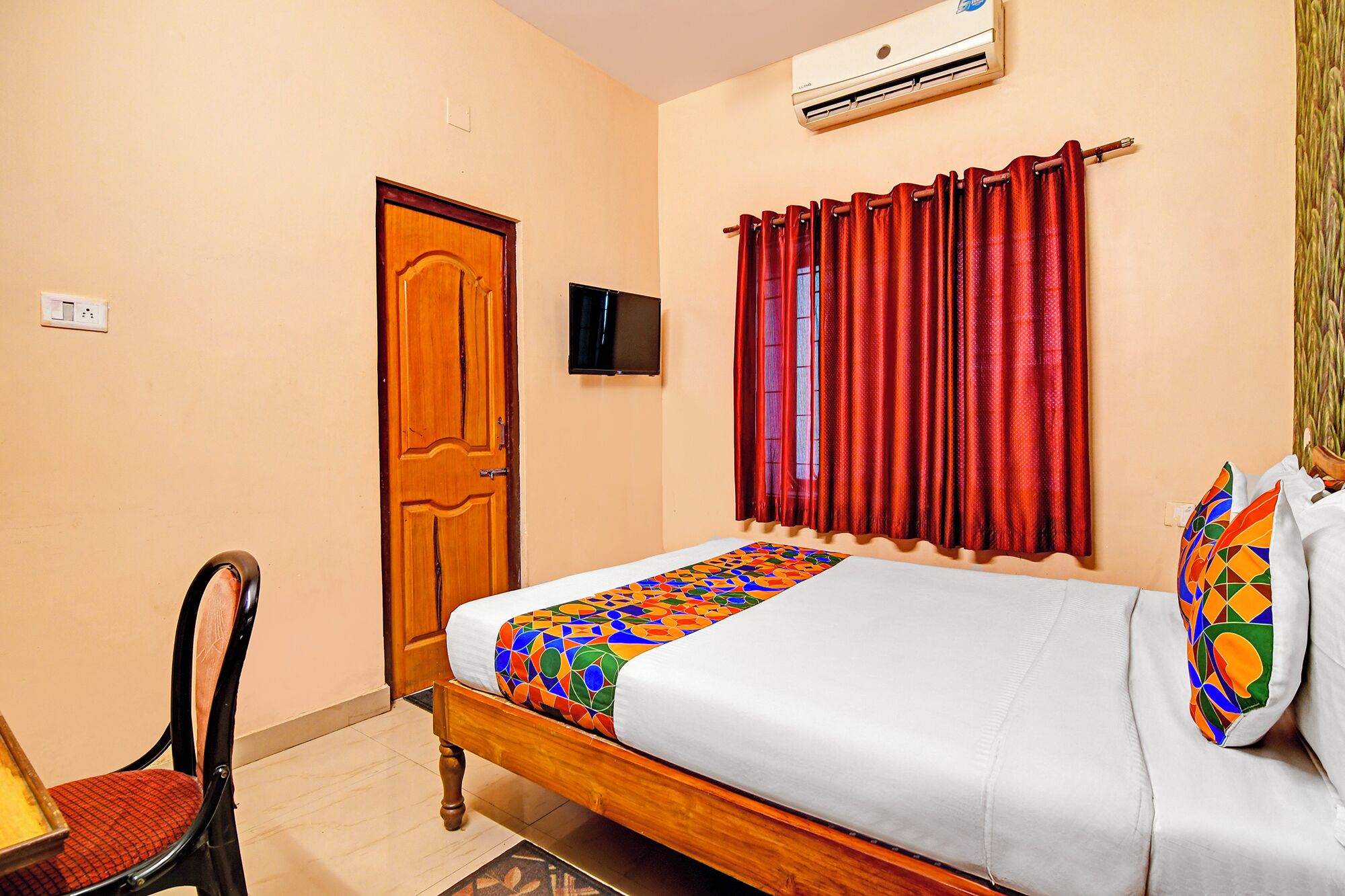 A bedroom with a wooden bed, a red curtain, a TV mounted on the wall, and a door.