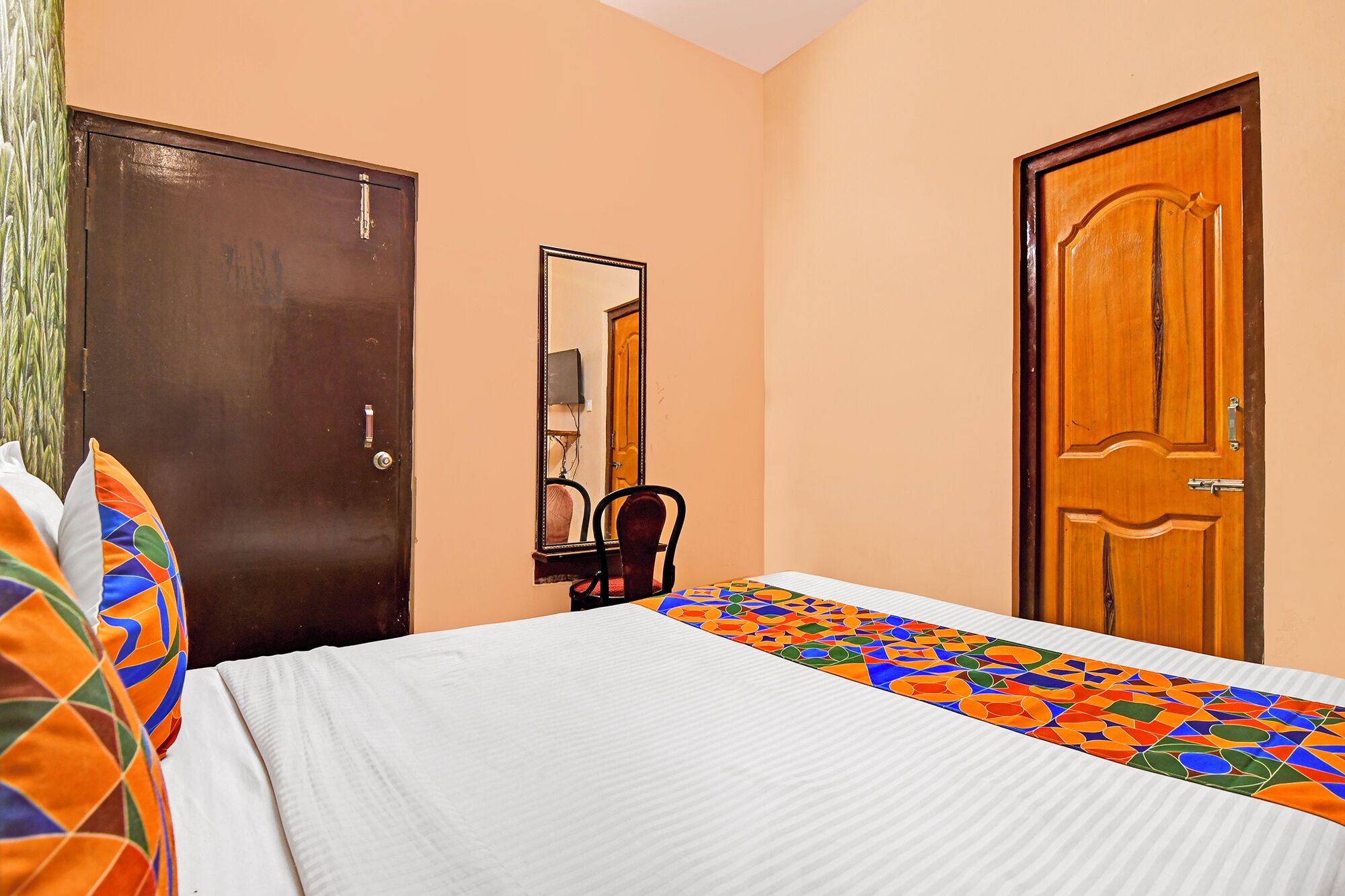 A bedroom with a bed, two doors, a chair, and a mirror.