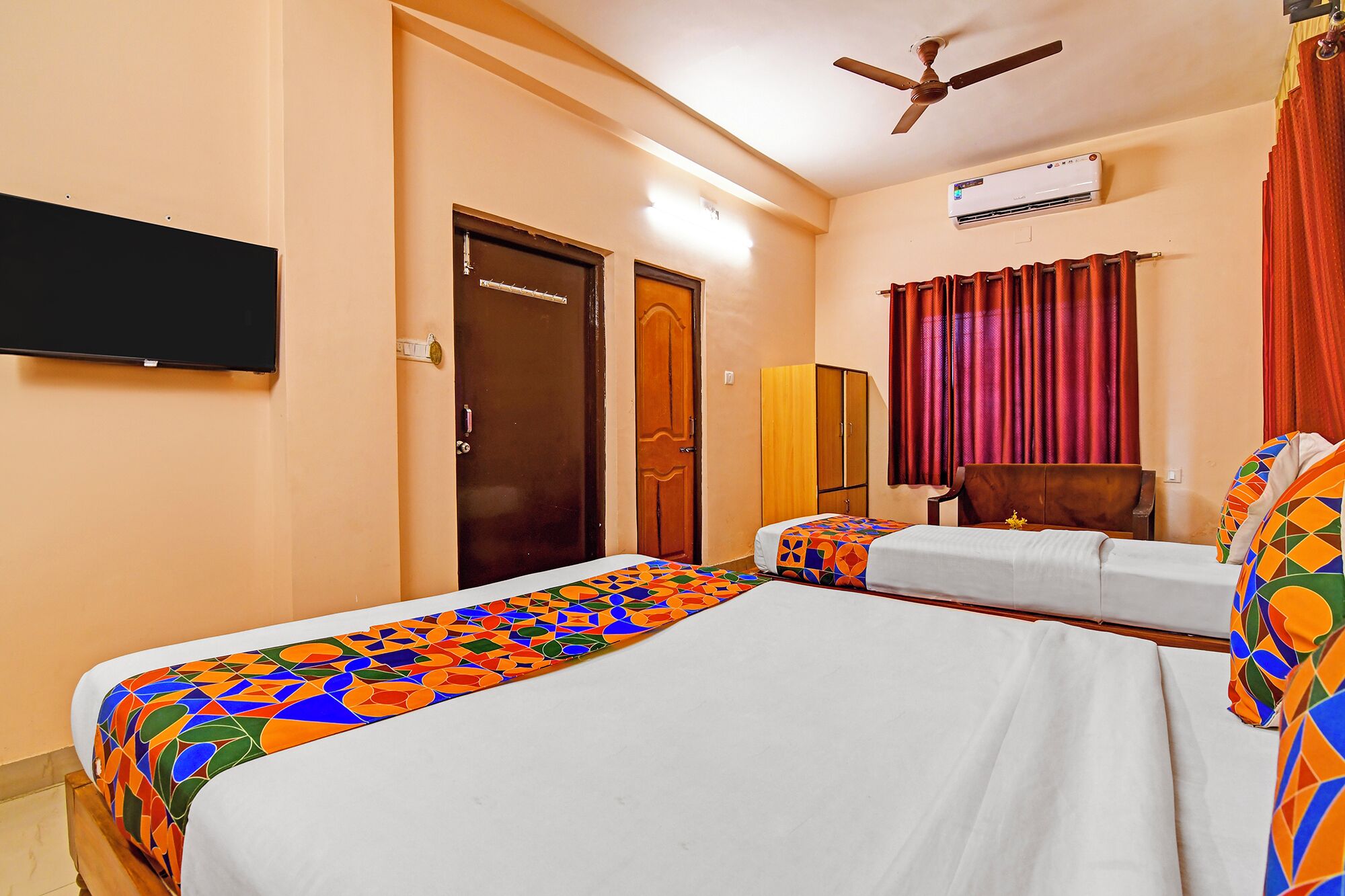 A hotel room with two beds, a ceiling fan, an air conditioner, and a TV mounted on the wall.