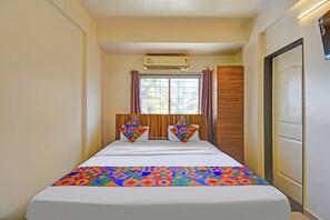 Una camera d'albergo con un letto, due cuscini, una finestra con tende, un condizionatore d'aria e una porta.