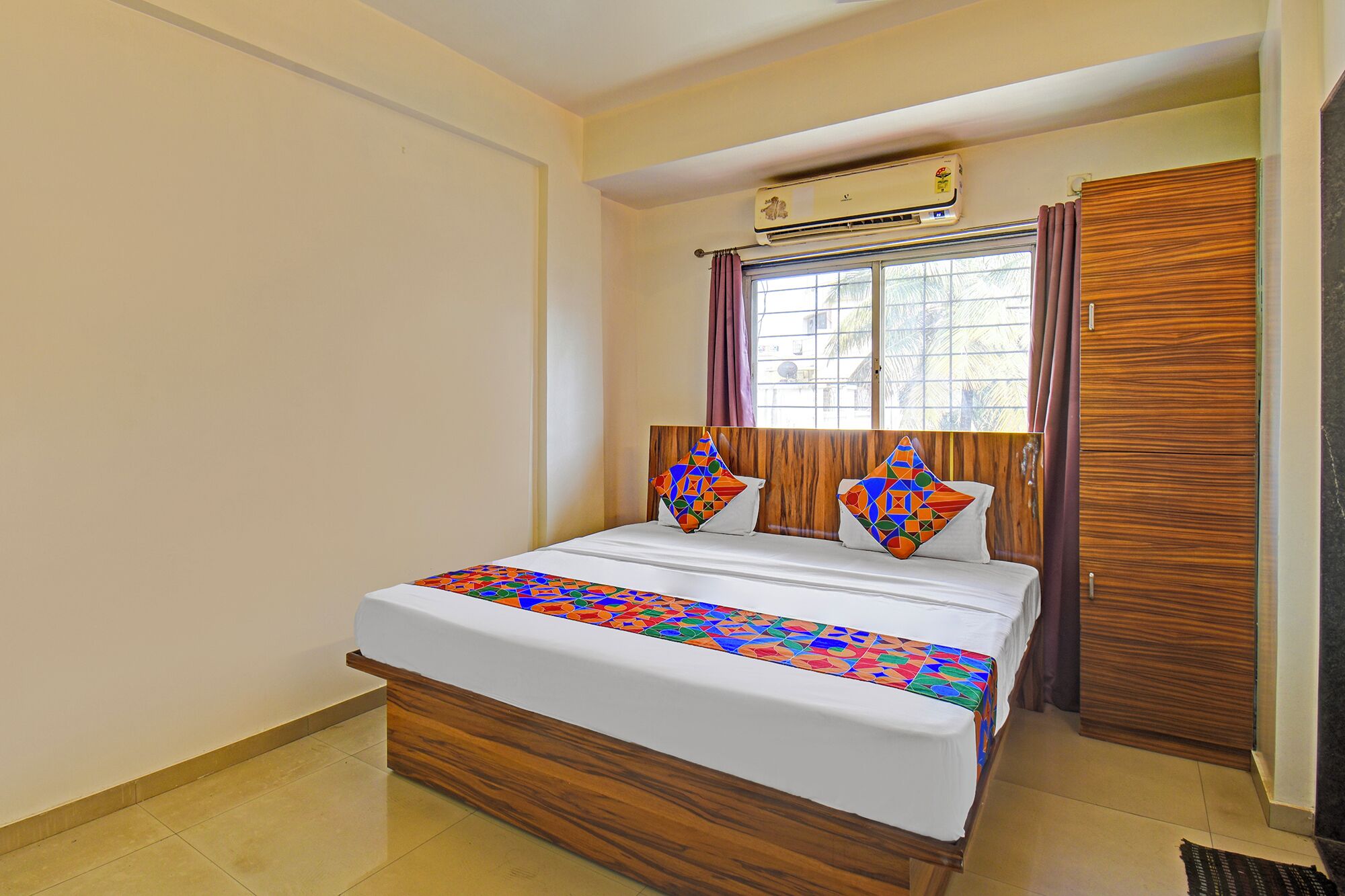 A bedroom with a wooden bed frame, a window with curtains, an air conditioning unit, and a wardrobe.