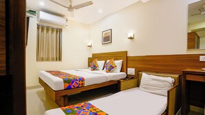 A hotel room with two single beds, a wooden headboard, a nightstand, a desk, a chair, a ceiling fan, an air conditioning unit, a window with curtains, and a wall-mounted light fixture. - Fabhotel Rahat (Mumbai)