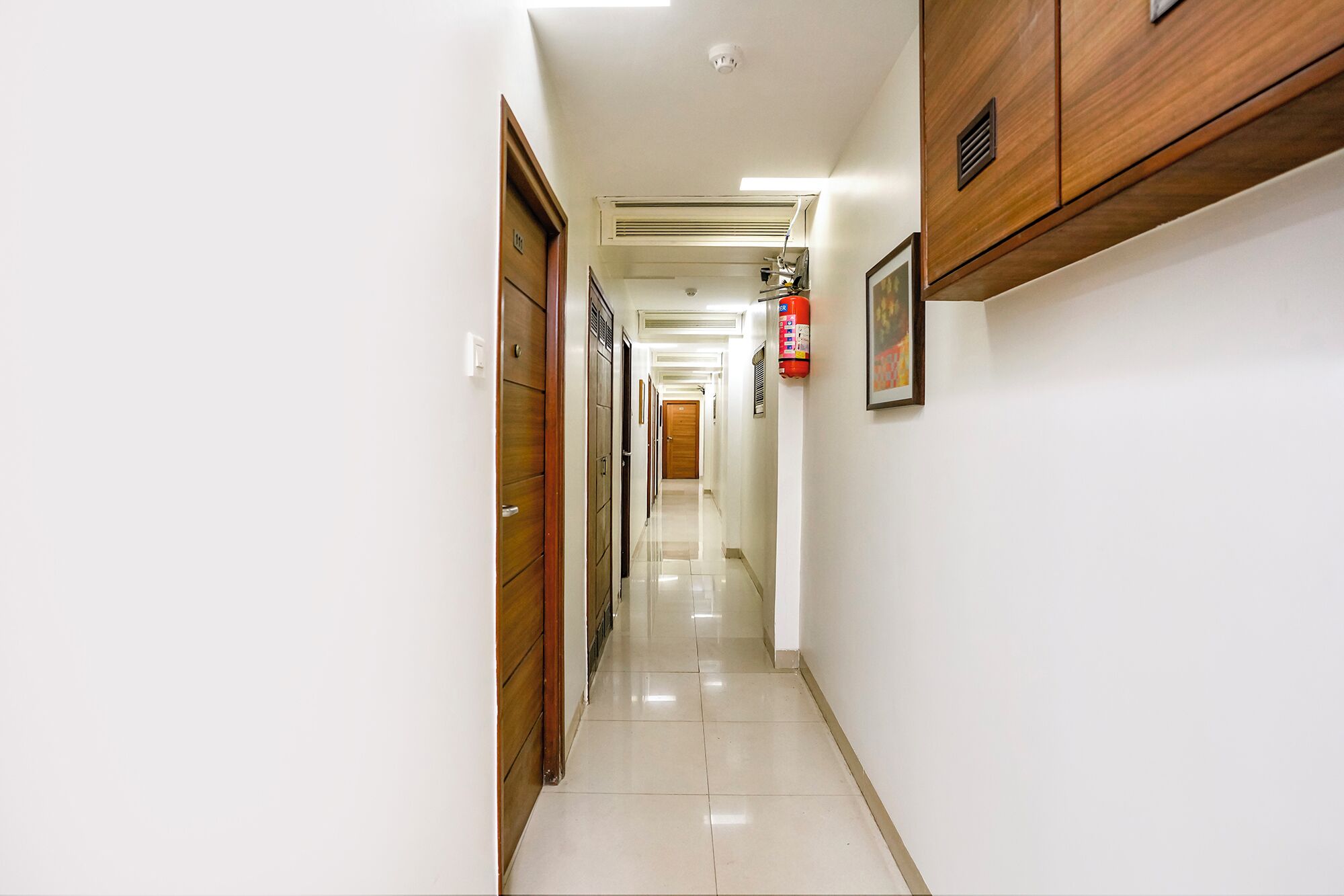 Un pasillo limpio y bien iluminado con puertas de madera y un extintor colgado en la pared.