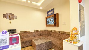 A modern living room with a brown sectional sofa, a glass coffee table, and a television mounted on the wall. - Fabhotel High View (Faridabad)