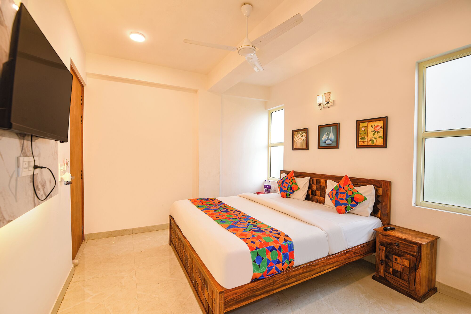 A bedroom with a wooden bed, a nightstand, a ceiling fan, and a TV mounted on the wall.