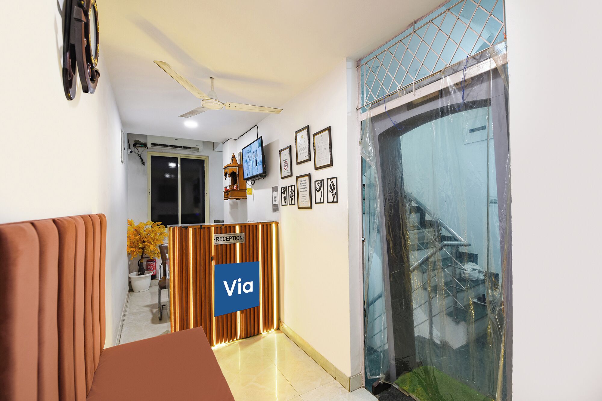 A reception desk with a 'Via' sign, a ceiling fan, framed certificates, and a large window with a view.