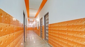 Een gang met betegelde muren en deuren, die uitkomt in een kamer met een bed en een raam.
