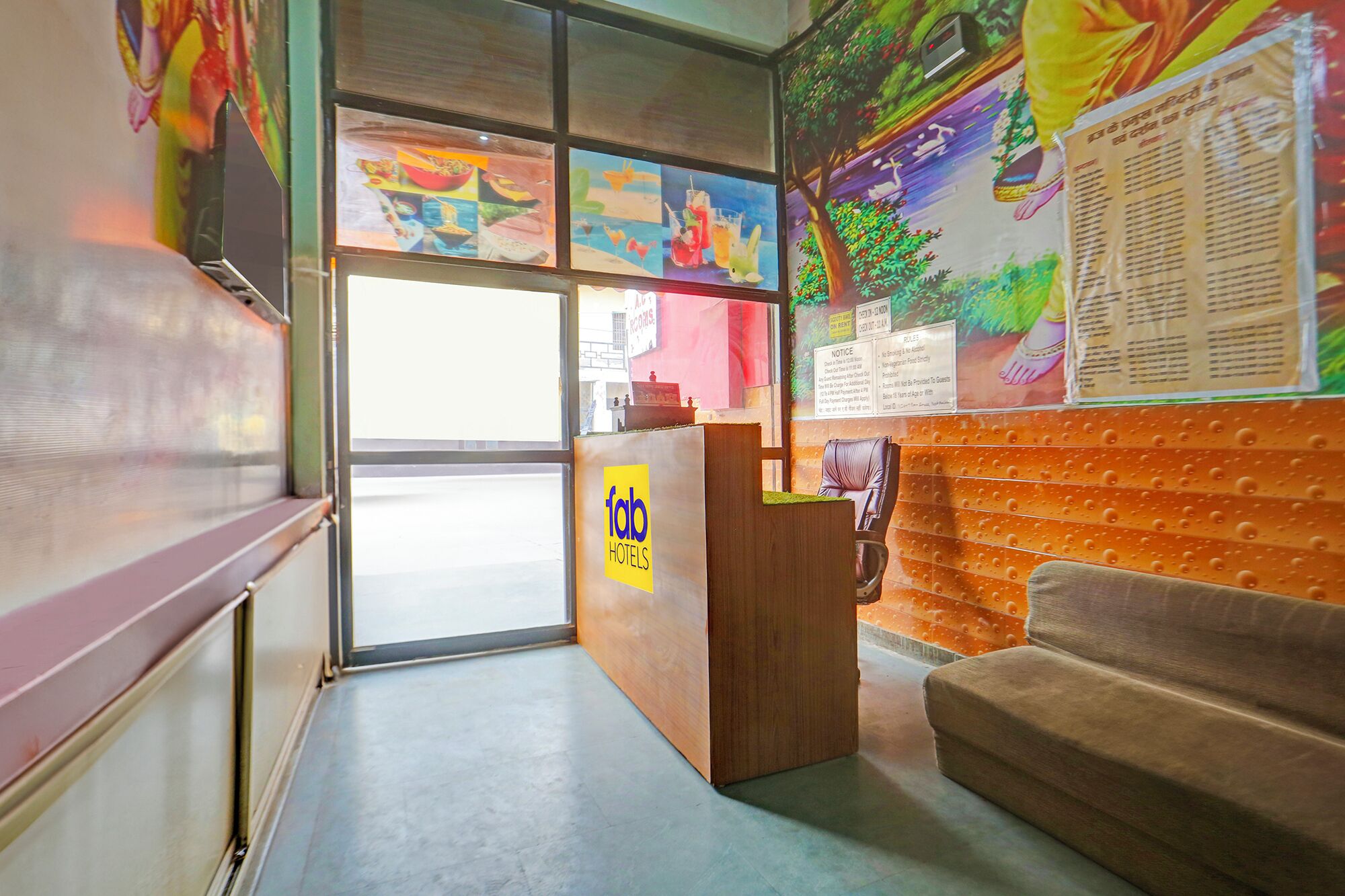 A hotel reception area with a wooden desk, a couch, and colorful artwork on the walls.