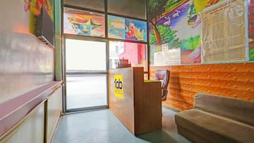 A hotel reception area with a wooden desk, a couch, and colorful artwork on the walls.