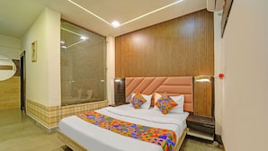 Una habitación de hotel con una cama grande, un cabecero de madera, una ventana con persianas y una mesita de noche pequeña.