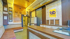 Zona de recepción de un hotel con un mostrador de madera, un área de descanso con bancos y un letrero en la pared que dice 'fab hotels'.