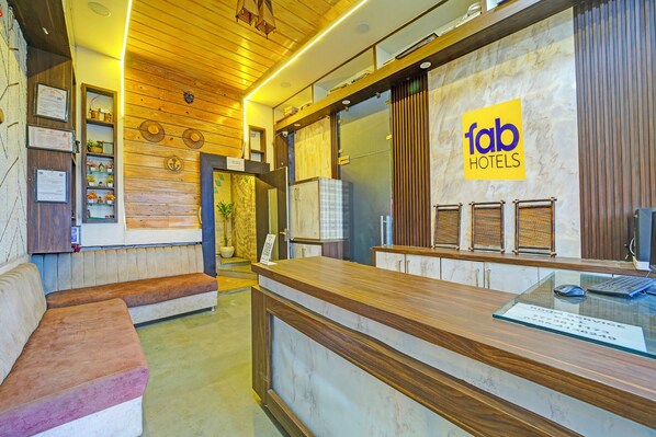 Een hotel receptie met een houten balie, een zithoek met banken, en een wandbordje met 'fab hotels'.