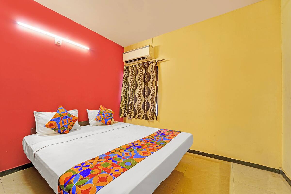 A hotel room with a bed, a red wall, a yellow wall, and an air conditioning unit.
