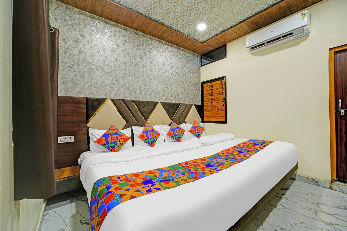 A hotel room with a bed, a headboard, a wall-mounted air conditioner, and a door.