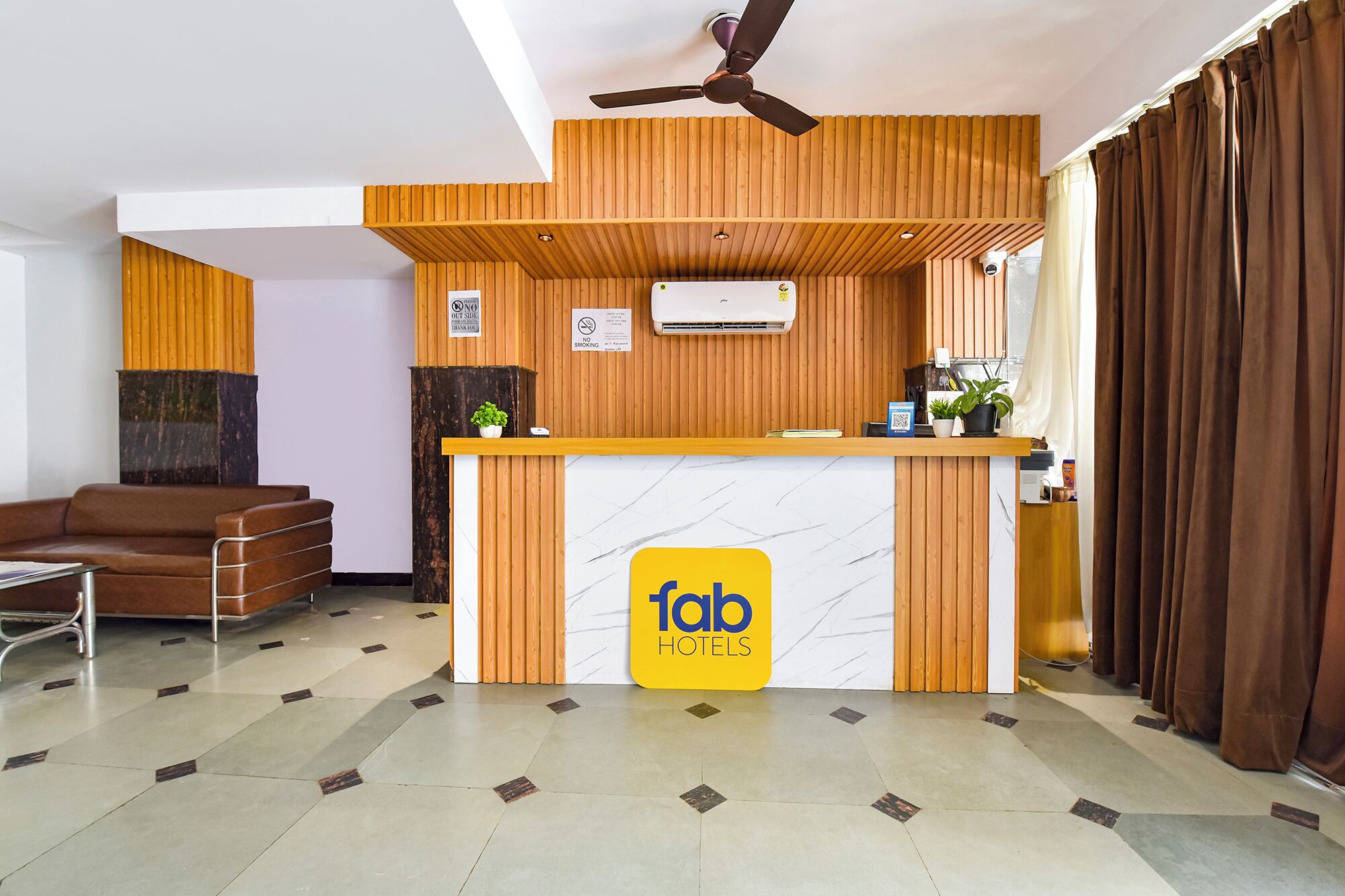 A reception desk with a 'fab hotels' sign, a ceiling fan, and a brown leather sofa in the background.