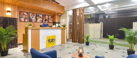 A hotel reception area with a wooden reception desk, a receptionist, and blue seating.