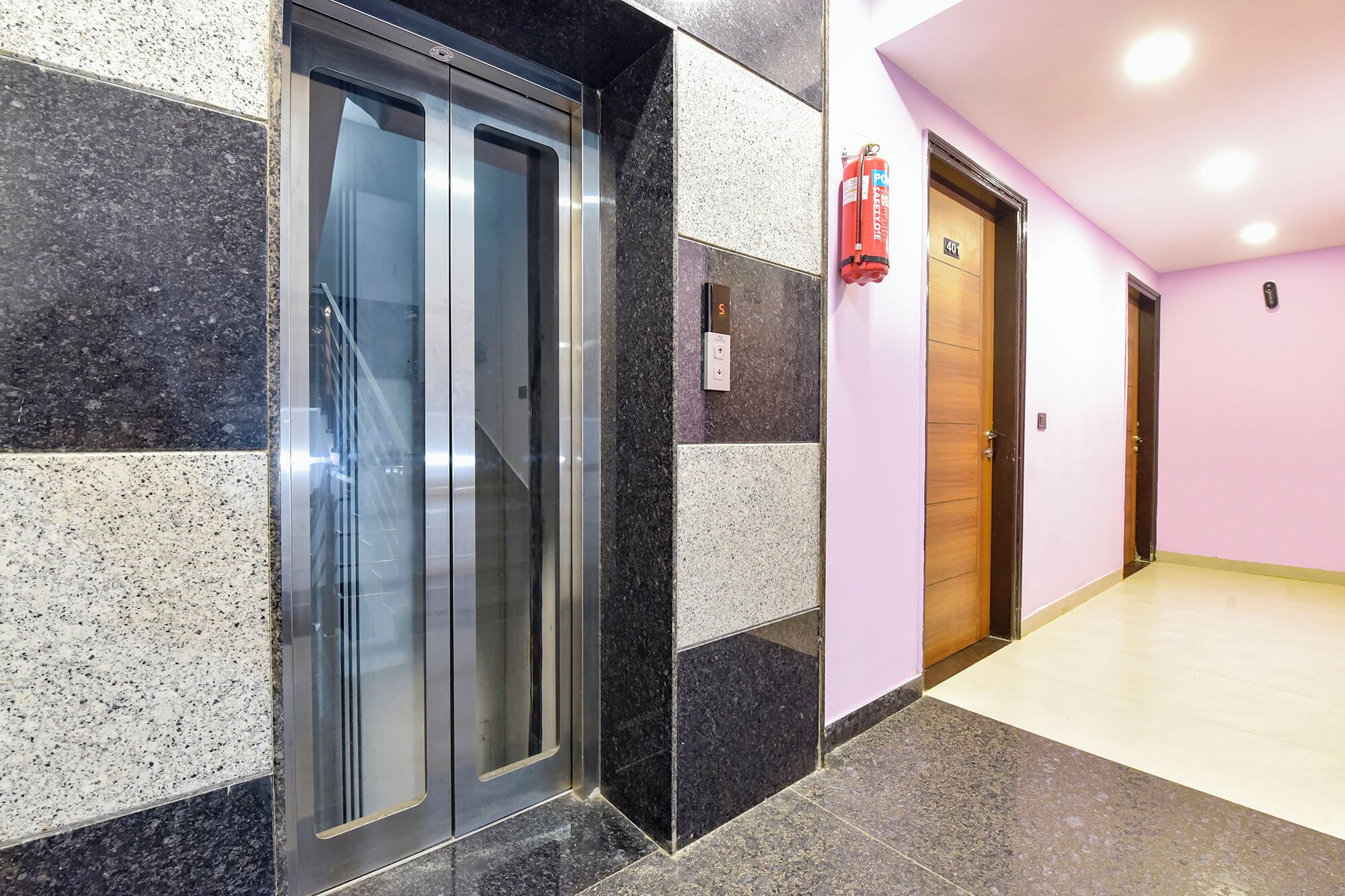 A modern elevator with a metallic finish, adjacent to a fire extinguisher mounted on the wall.