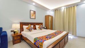 A neatly arranged hotel room with a wooden bed, a nightstand with a lamp, a wardrobe, and a large window with curtains. - Fabhotel Pink Palace Raja Park (Jaipur)
