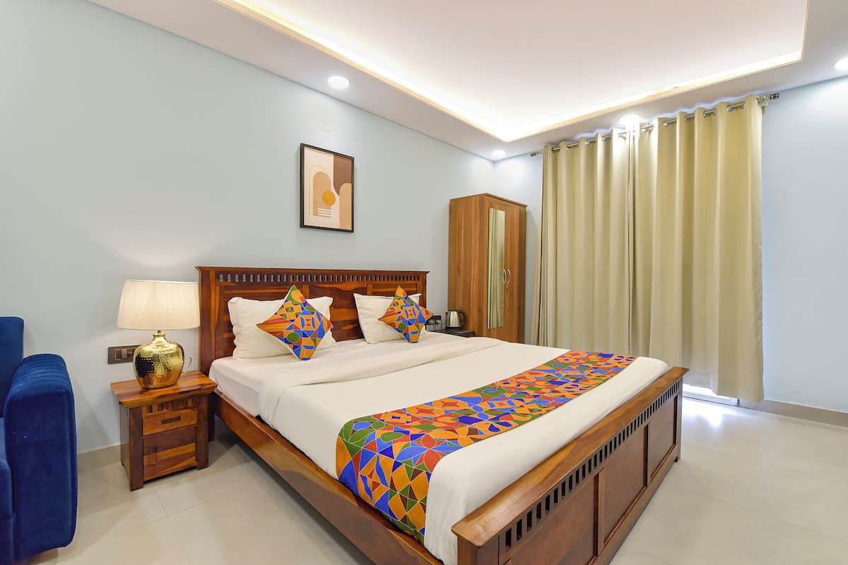 A neatly arranged hotel room with a wooden bed, a nightstand with a lamp, a wardrobe, and a large window with curtains.