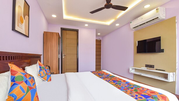 A hotel room with a bed, a ceiling fan, recessed lighting, an air conditioning unit, a television mounted on the wall, and a door.