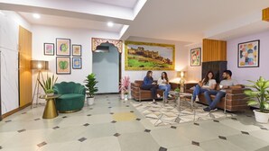 A modern living room with a green sofa, a brown sofa, and a coffee table. There are framed pictures on the walls and a large painting above the brown sofa. - Fabhotel Pink Palace Raja Park (Jaipur)