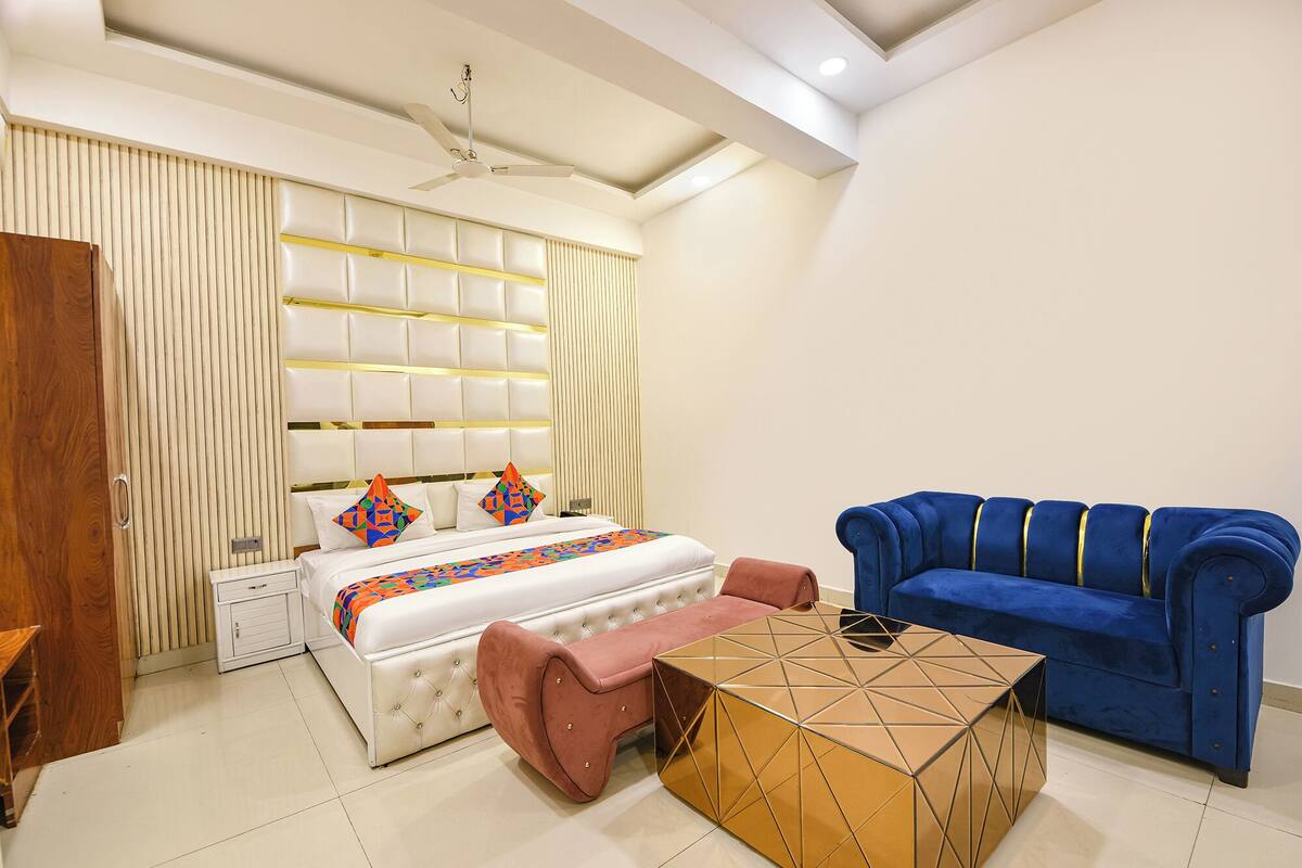 A bedroom with a bed, a blue sofa, a pink chair, and a geometric coffee table.